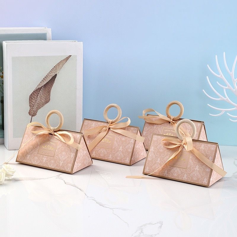 四個優雅的淡粉色禮盒，飾有幾何圖案，配有木質環形提手和米色絲帶。