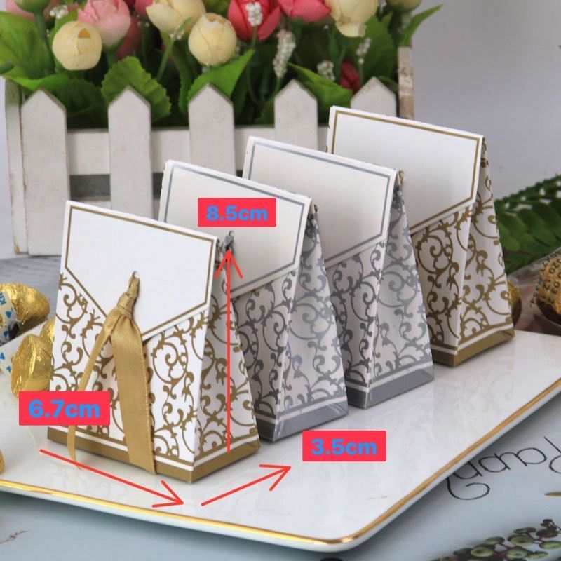 四個裝飾精美的紙質禮品盒，飾有金色或銀色的鏤空圖案和絲帶，擺放在白色托盤上。