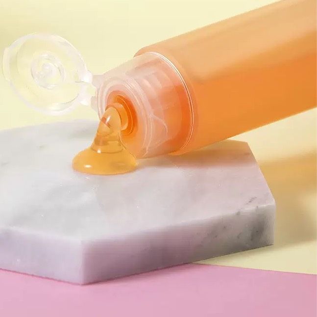 一管橙味凝膠放在大理石六角形上,一滴凝膠滴落在石頭表面。