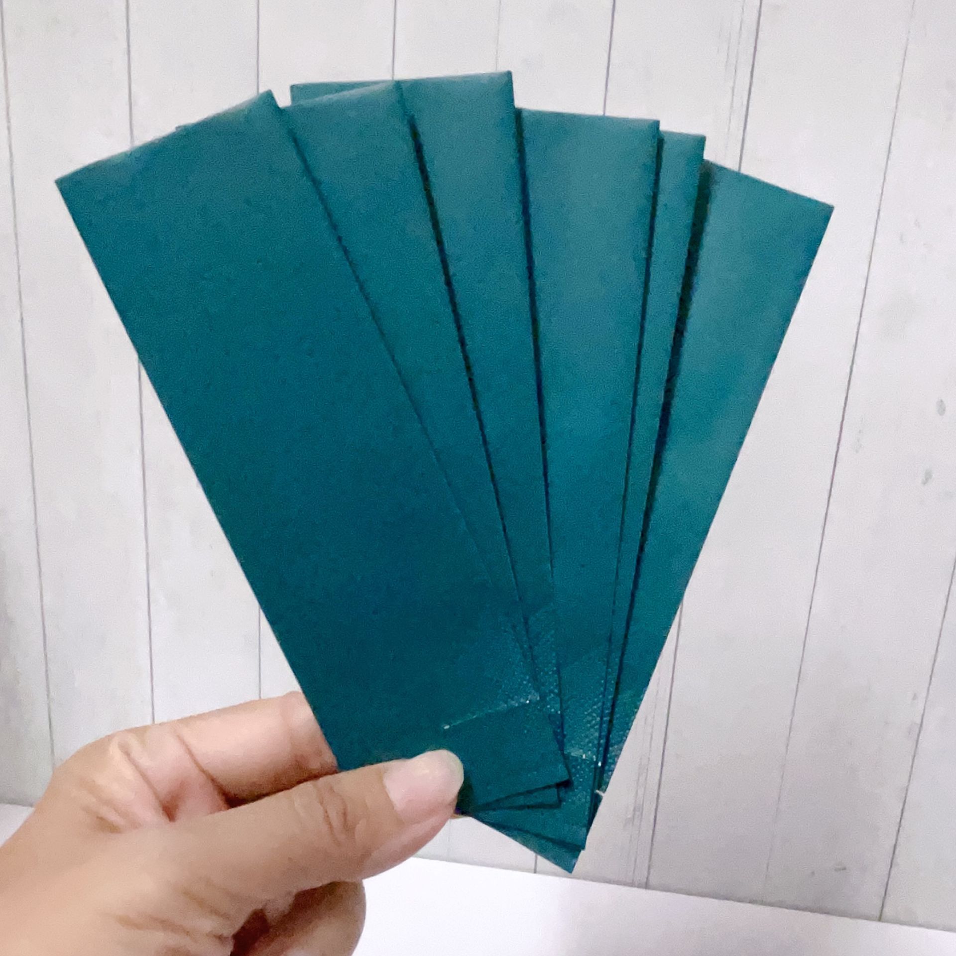 一隻手在白色木板背景上展開五個一模一樣的細長藍綠色信封。