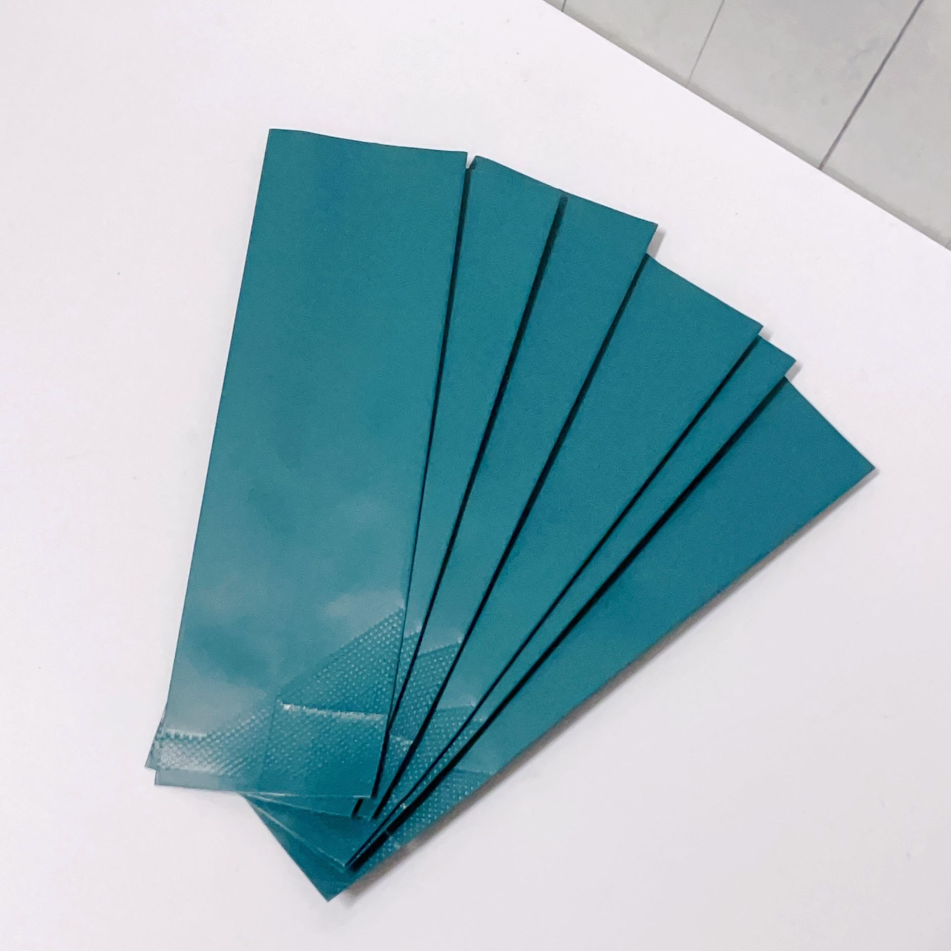 一隻手在白色木板背景上展開五個一模一樣的細長藍綠色信封。