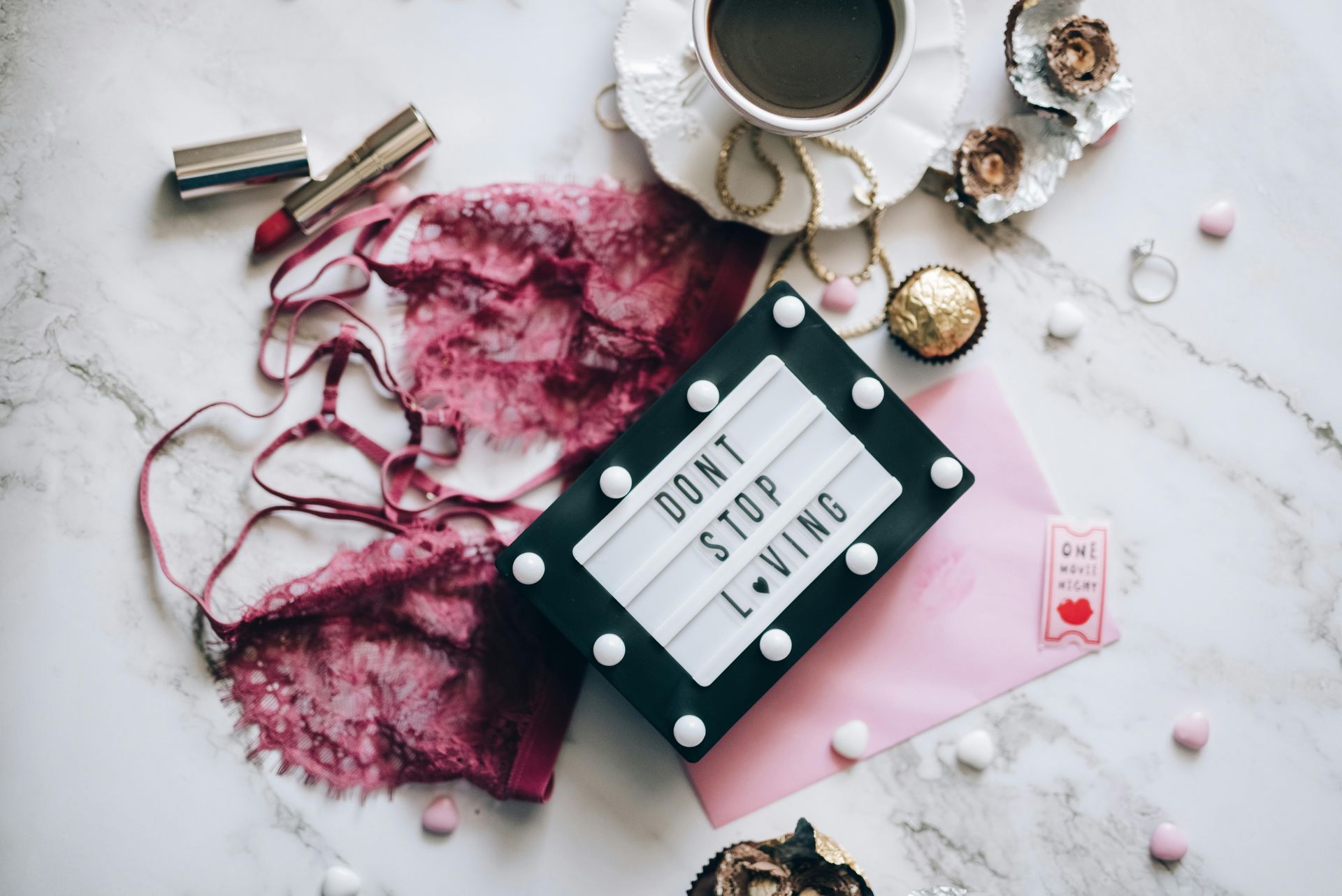 大理石檯面上擺放著一個寫著「不要停止愛」的燈箱，旁邊還有蕾絲內衣、咖啡杯、口紅和巧克力。