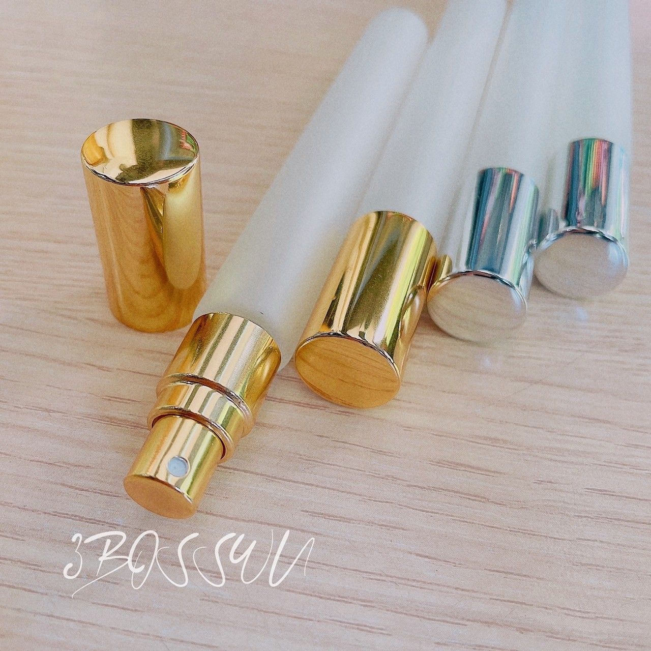 幾個磨砂玻璃噴霧瓶，配有金色和銀色瓶蓋，擺放在淺色木質表面上。