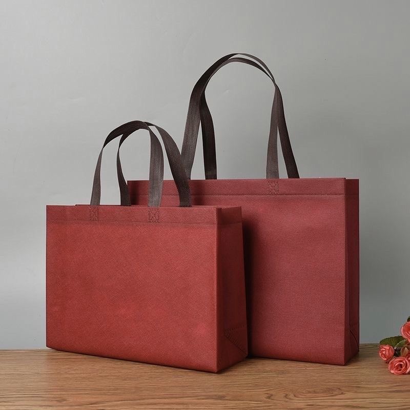 兩個大小不同的長方形深紅色不織布手提袋並排放置在木質表面上。