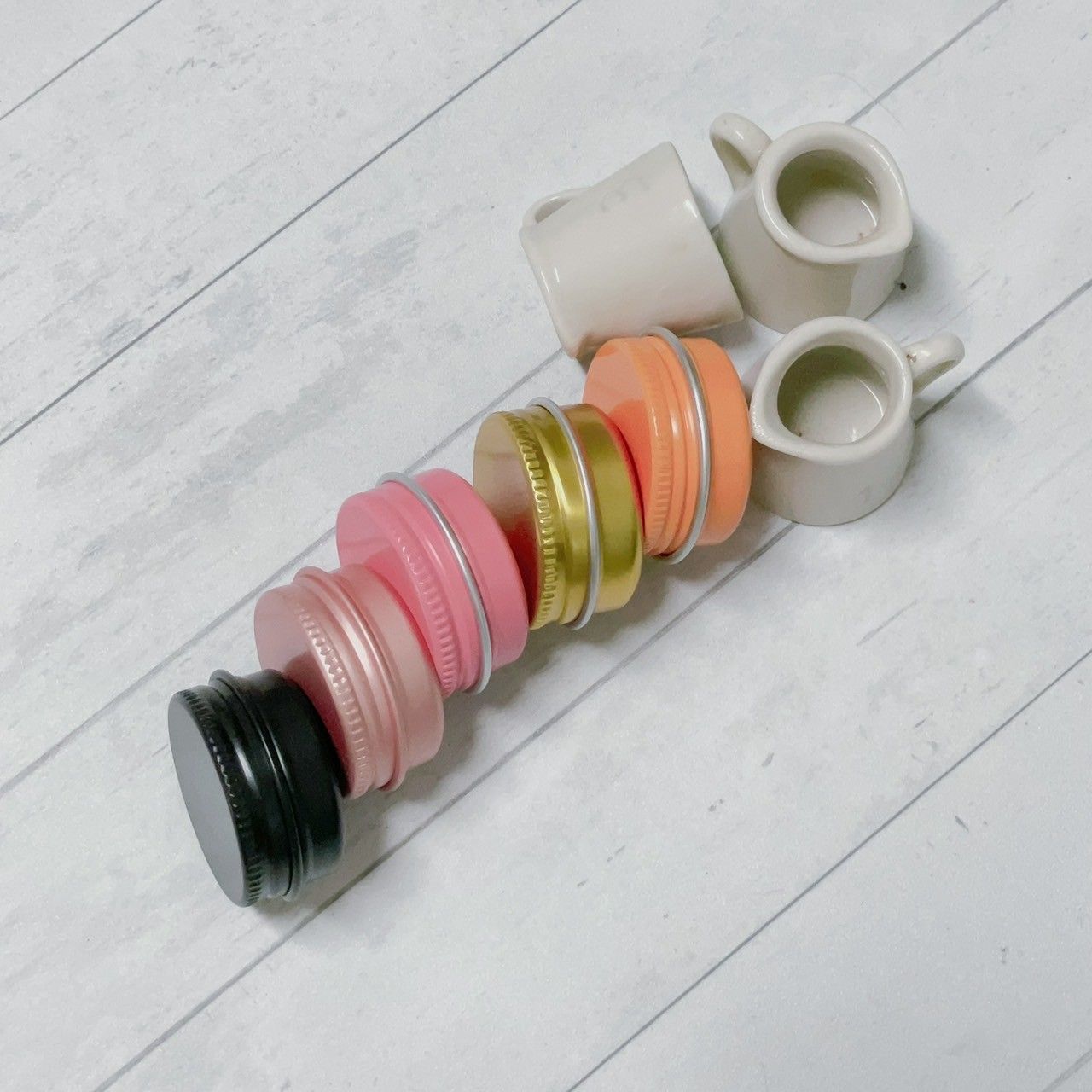 白色木板上擺放著一排色彩鮮豔的圓形錫罐，旁邊還有兩個小陶瓷罐。