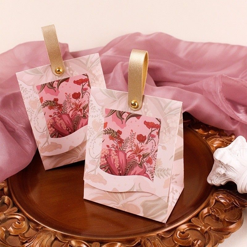 兩個飾有粉紅色花卉圖案和金色皮革質感提手的禮品袋，放在一個圓形的復古青銅色盤子上。