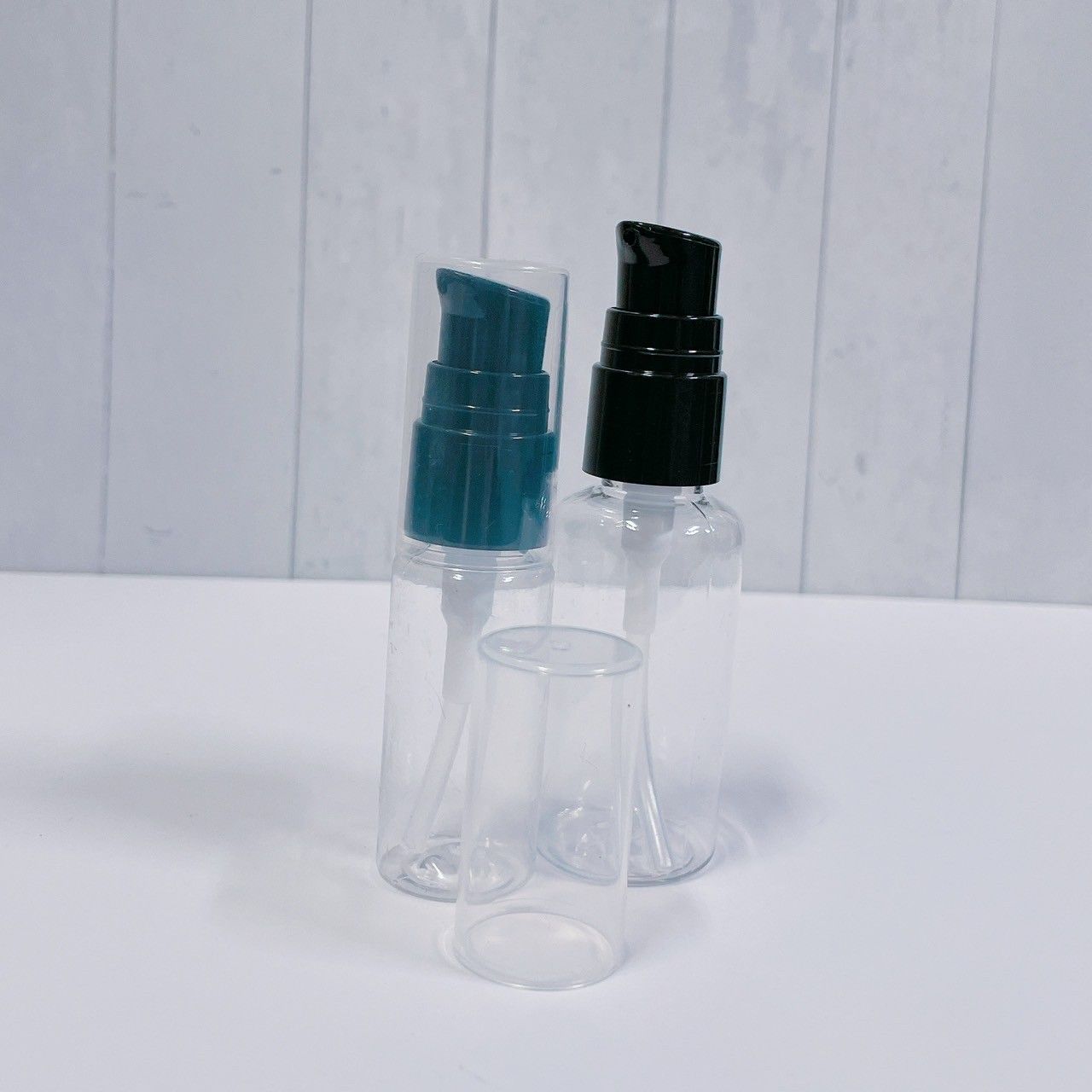 兩個透明塑膠按壓瓶放在白色表面上，一個配有青色泵頭，另一個配有黑色泵頭，瓶蓋鬆動。