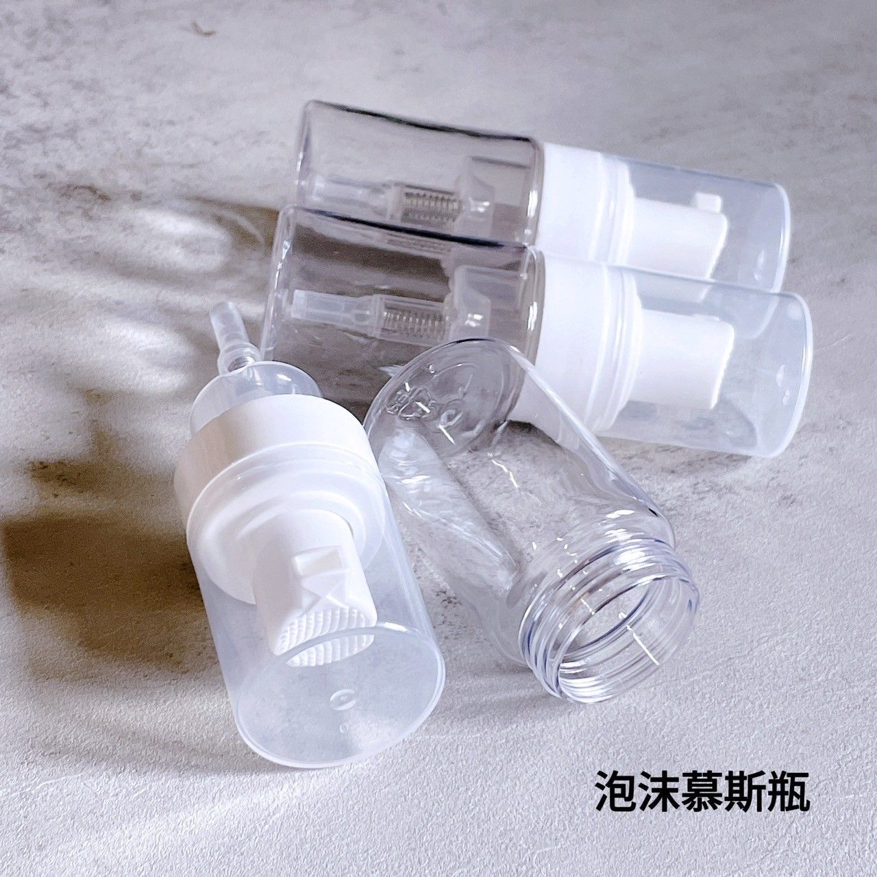 灰色表面上擺放著透明塑膠泡沫泵瓶，用於盛裝護膚品。