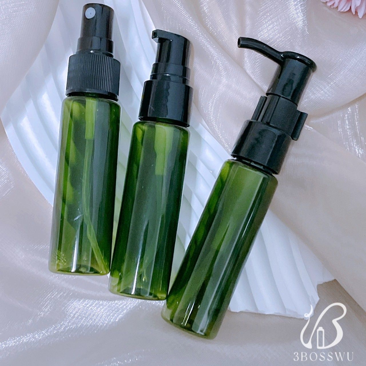三個小巧的半透明綠色圓柱形瓶子，配有黑色泵頭和噴霧蓋，擺放在一塊輕盈的紋理織物上。