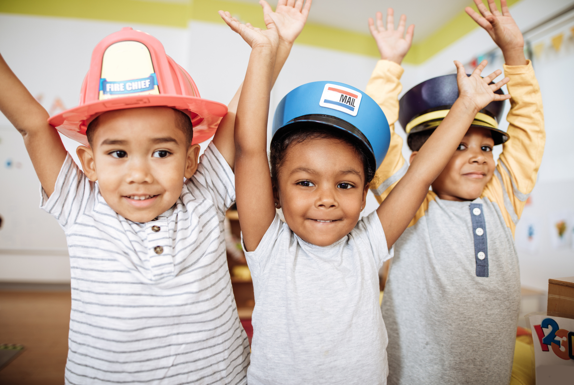 Three young boys wearing hats with their hands in the air.