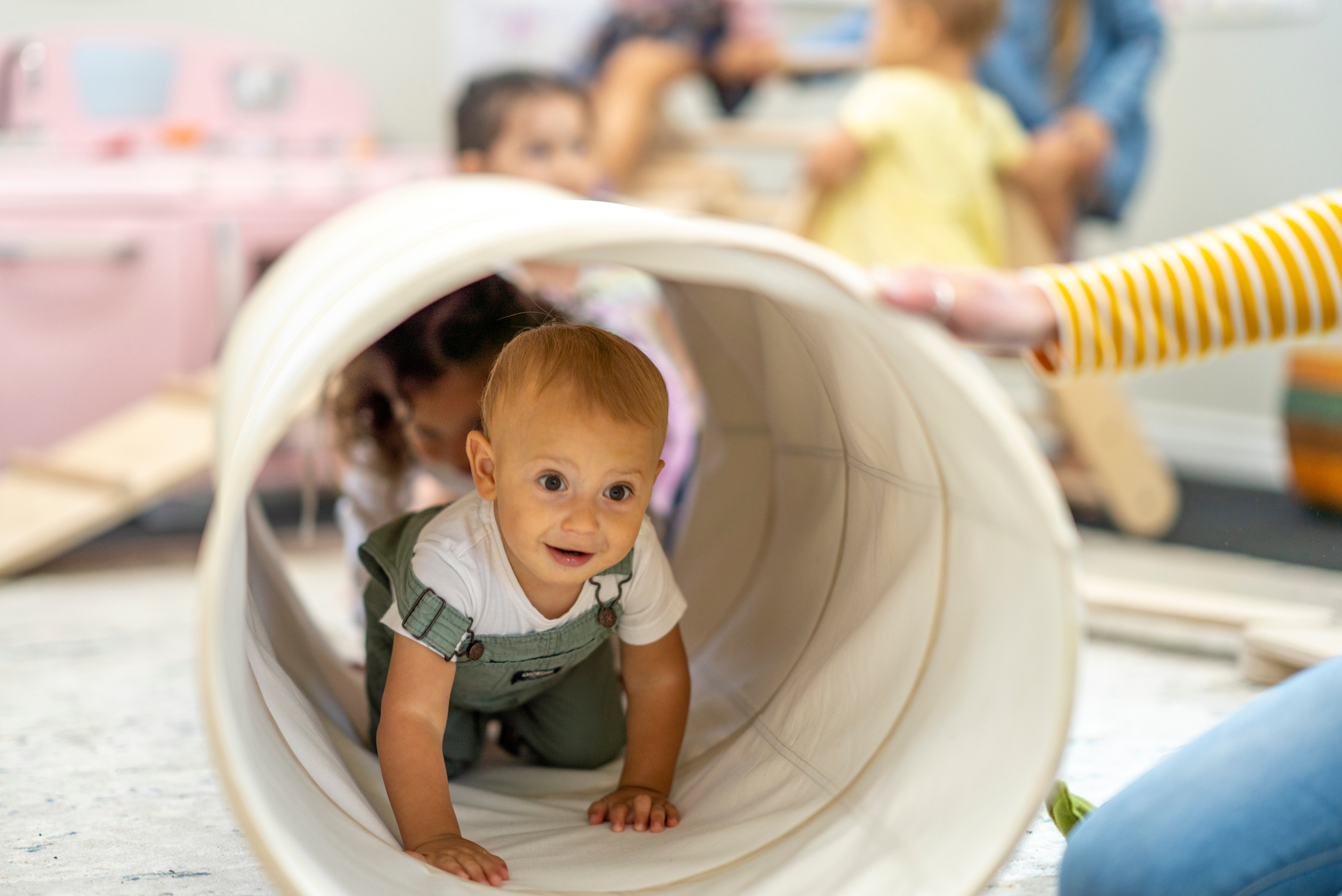 A baby is crawling through a tunnel in a play room.