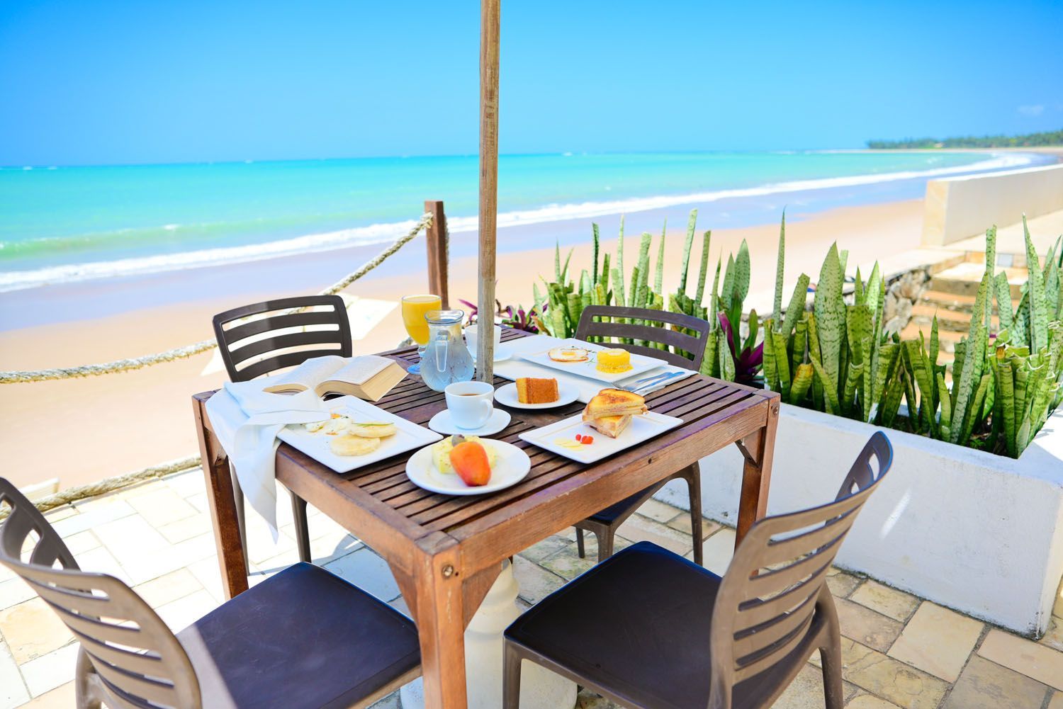 Uma mesa com pratos de comida está na praia.