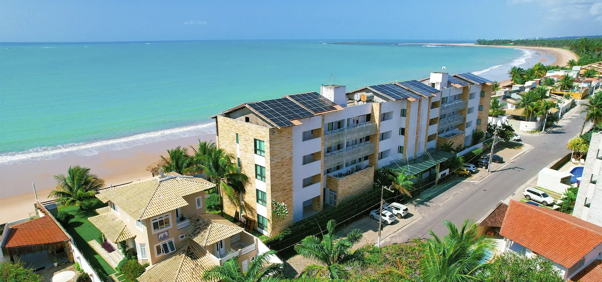 Um grande edifício com painéis solares no telhado fica próximo a uma praia.