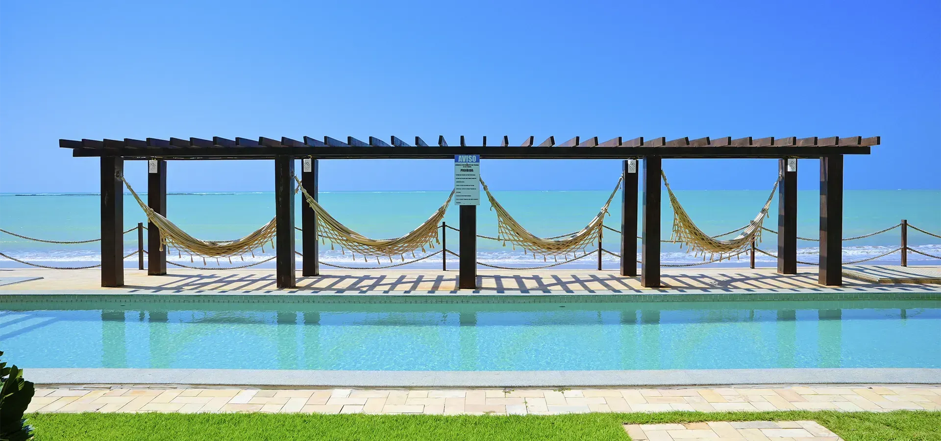 Uma piscina com redes penduradas e o mar ao fundo