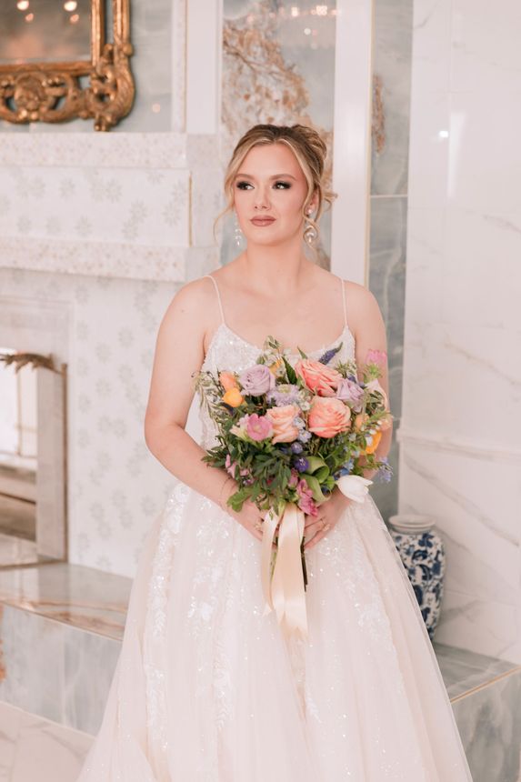 A bride in a wedding dress is sitting at a long table holding a bouquet of flowers.