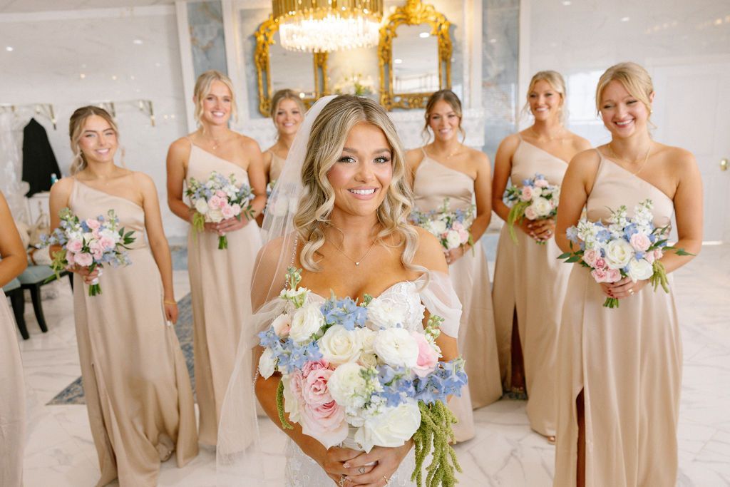 A woman is sitting in front of a large mirror in a room with a wedding dress hanging on the wall.