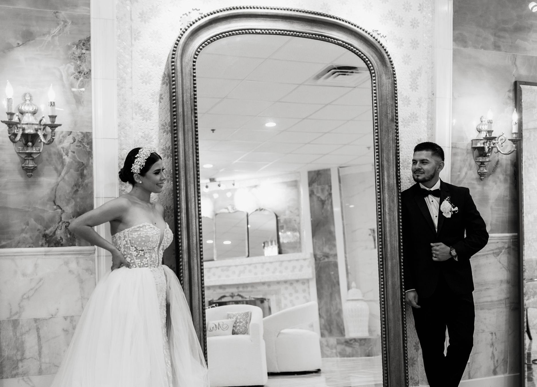 a bride and groom are standing in front of a large mirror .