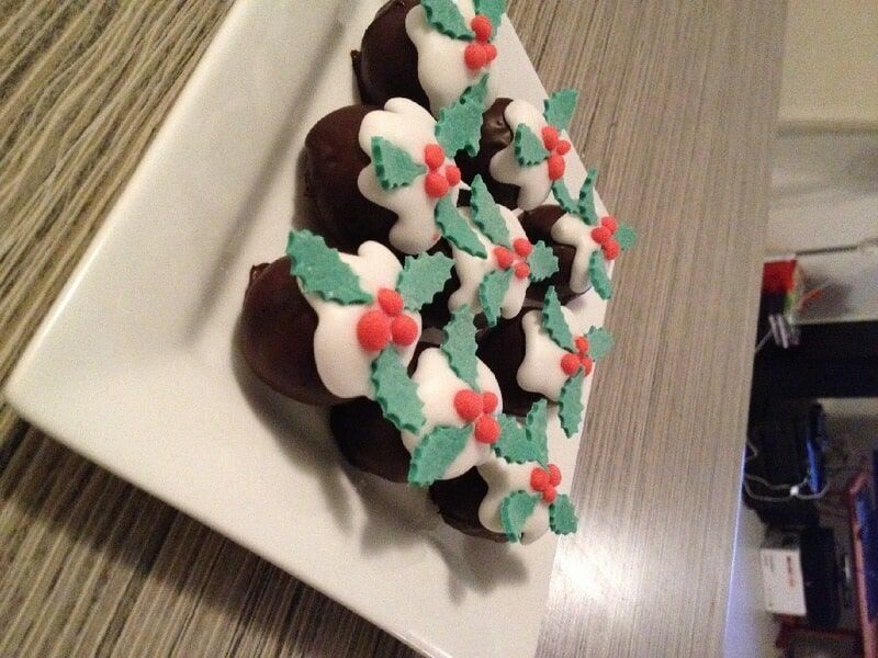 A White Plate Topped With Chocolate Balls Decorated With Holly