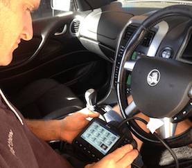 A Man is Sitting in the Driver 's Seat of a Car Using a Tablet — Mechanical Repairs In Gympie, QLD