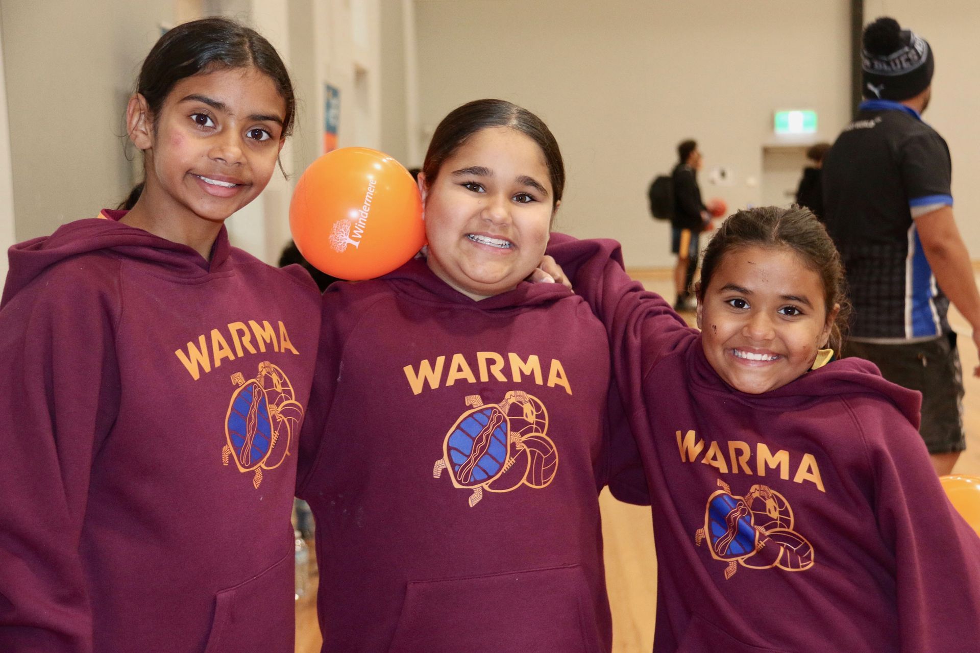 A young person with painted hand displaying the Aboriginal flag, smiling. They have ochre face paint and curly hair.
