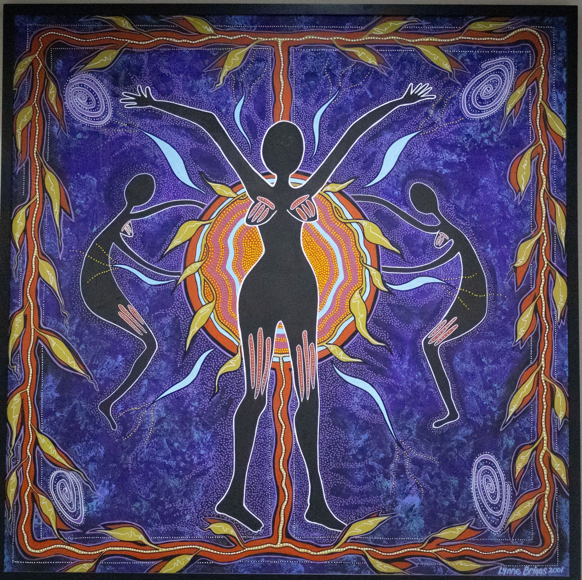 Aboriginal artwork: central black figure with arms raised, surrounded by two figures, all against a purple background with a sunburst and leaf border.