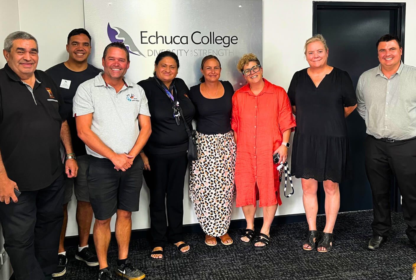 Group of nine people standing in front of an Echuca College sign. They are smiling, and some are wearing casual attire.