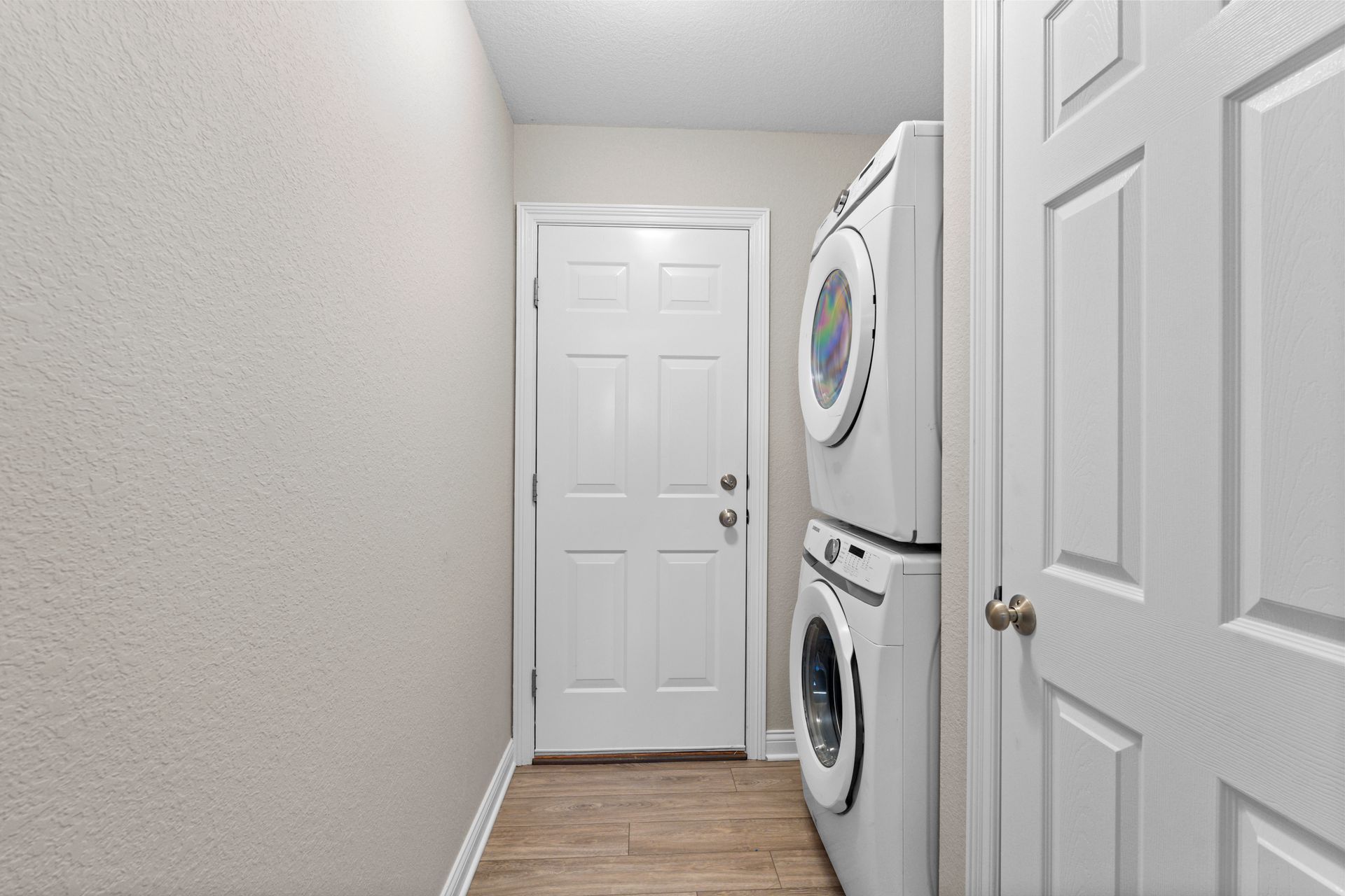 Laundry room with stacked white washer and dryer, white door, and beige walls.