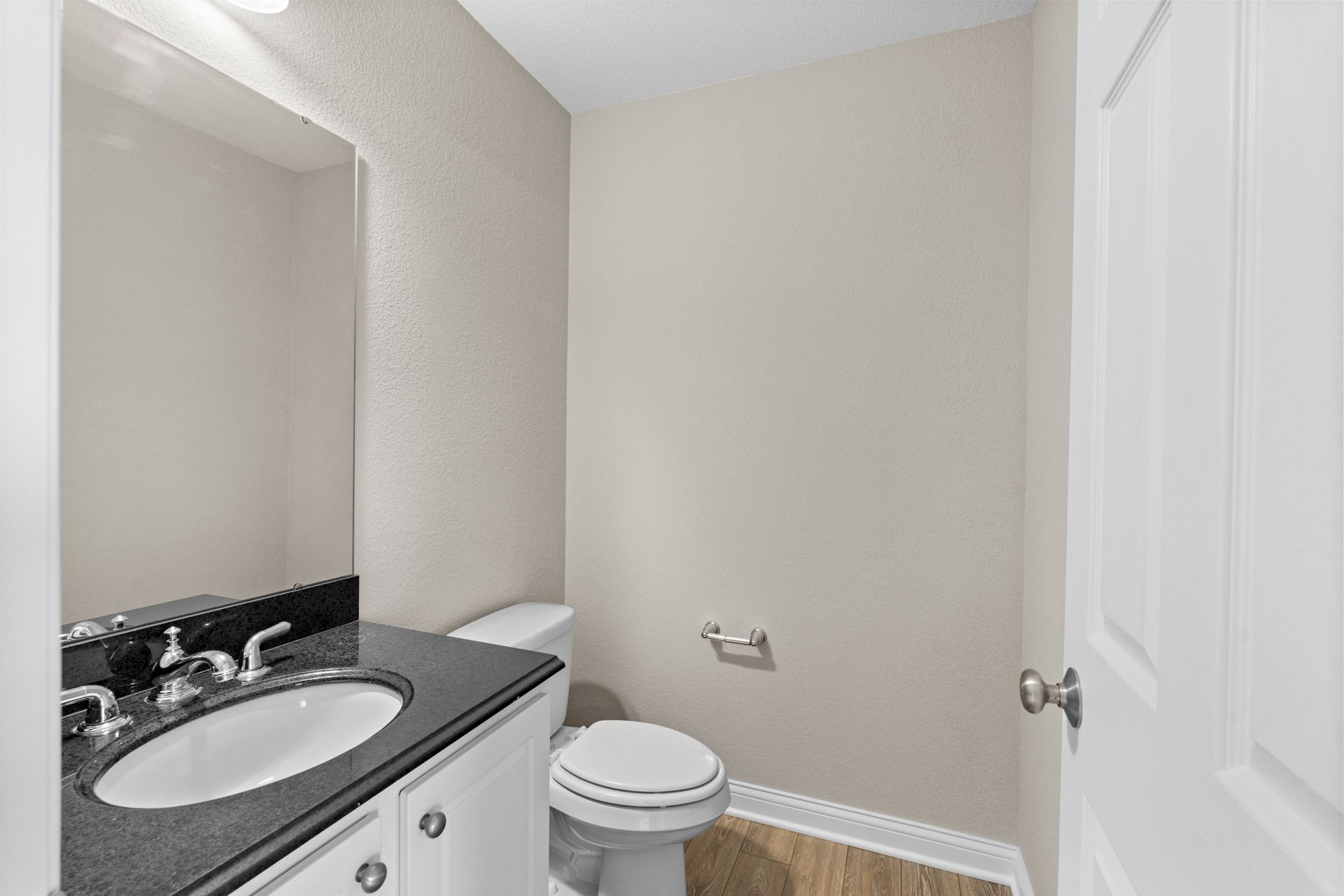 Small, neutral-toned bathroom with toilet, sink, mirror, and closed door.