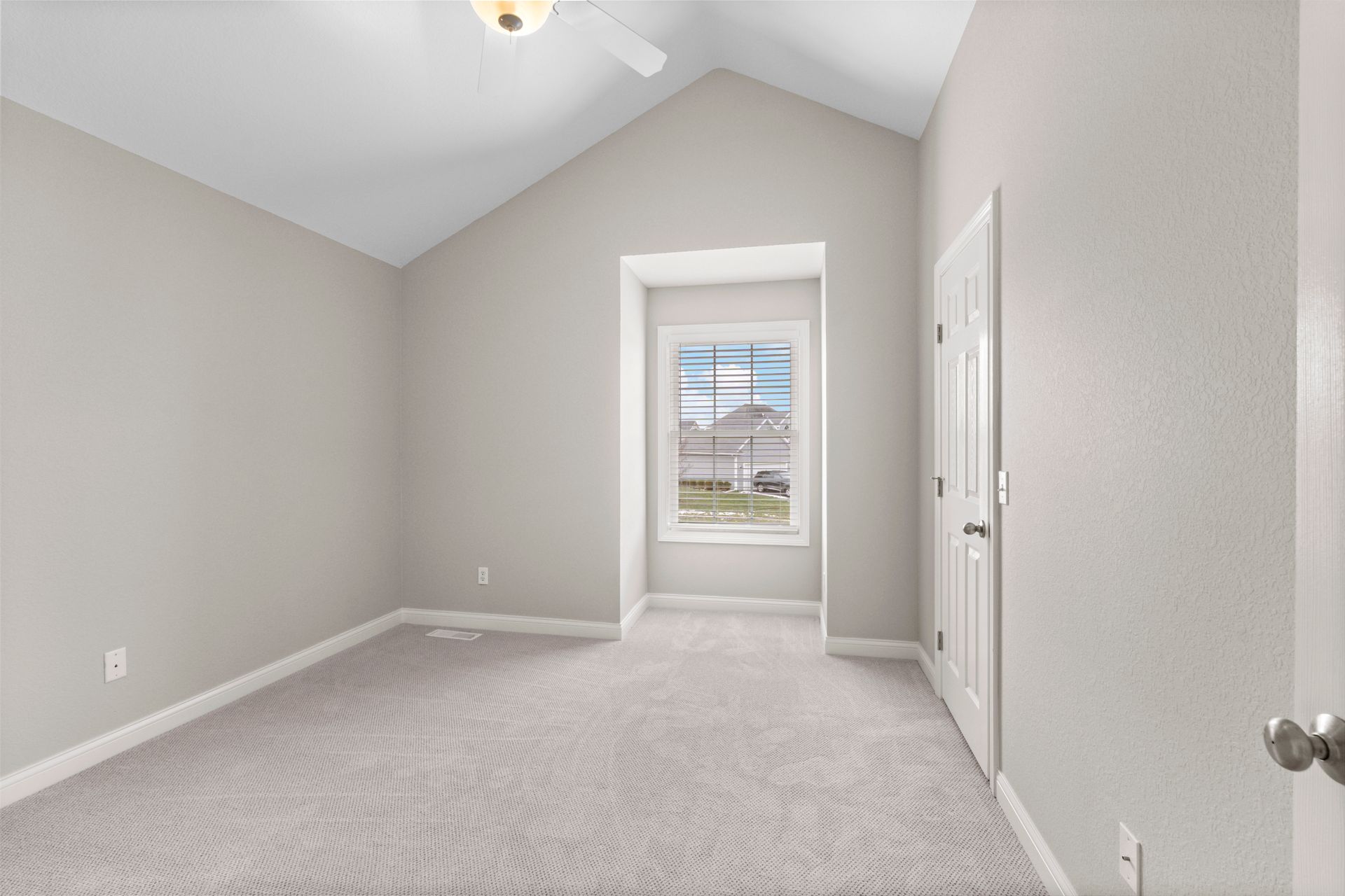 Empty bedroom with gray walls, carpet, window, and white door.