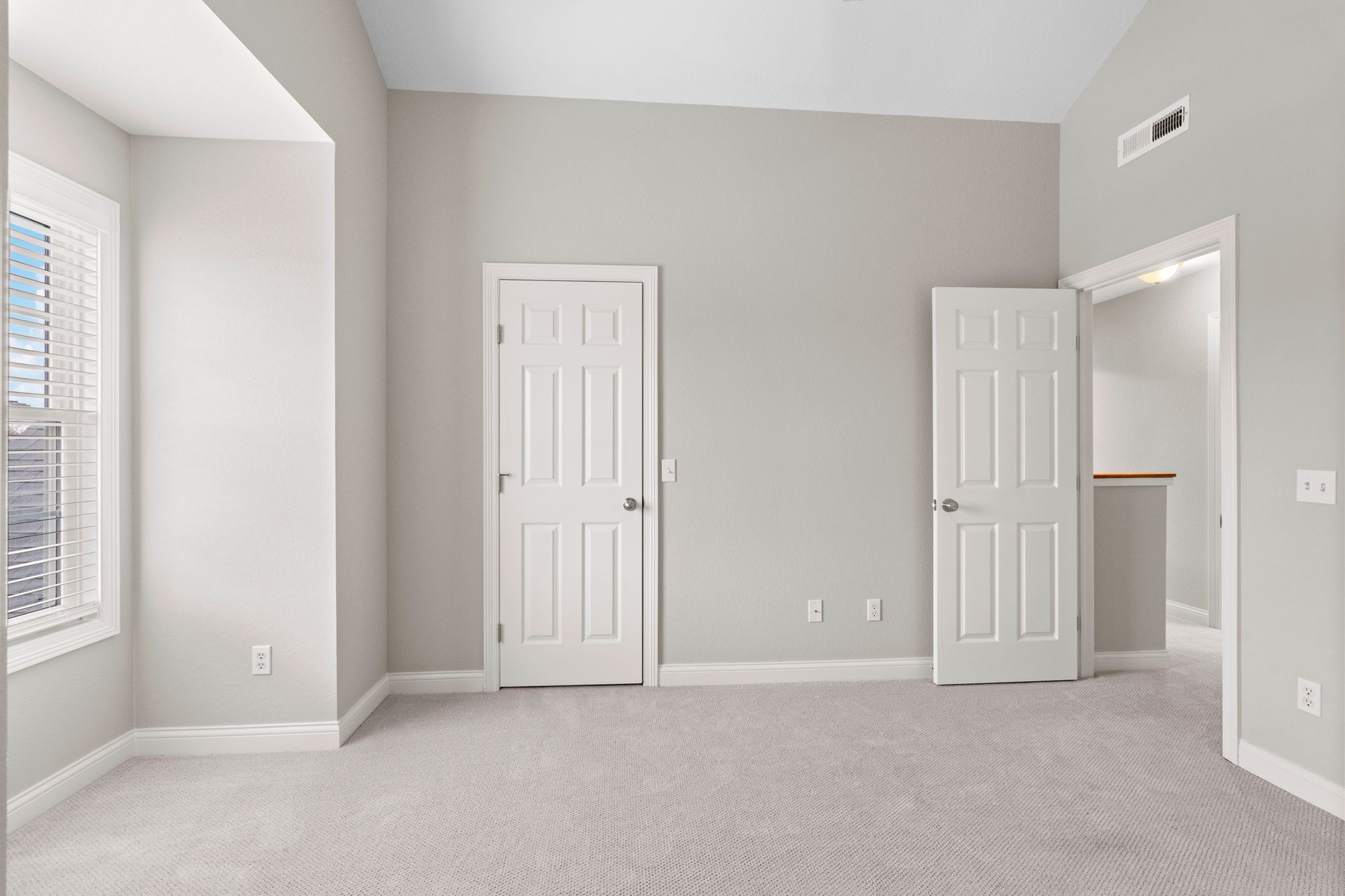 Empty bedroom with gray walls, white doors, window, and carpet.