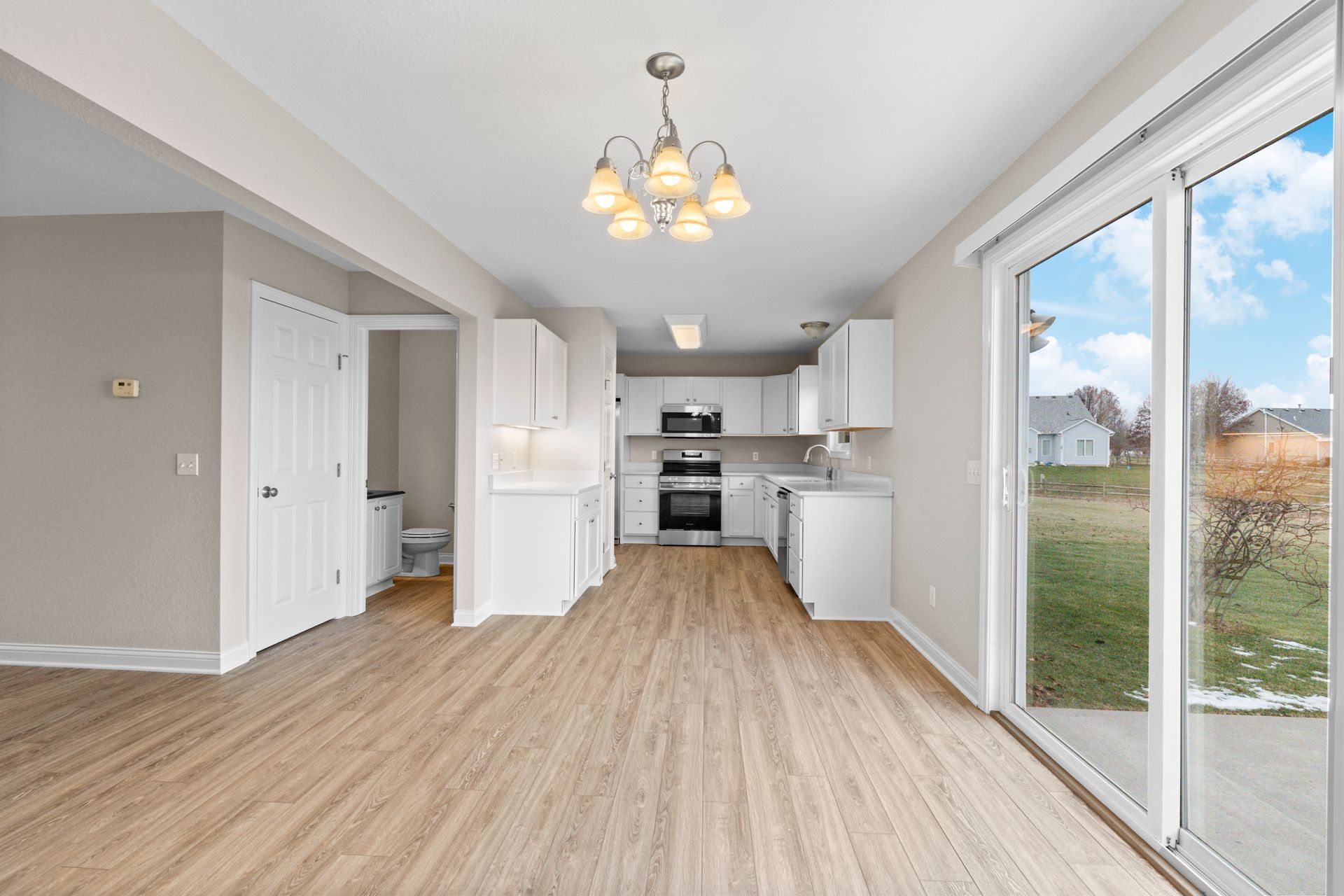 Light-filled kitchen with white cabinets, wood-look flooring, and sliding glass door to backyard.