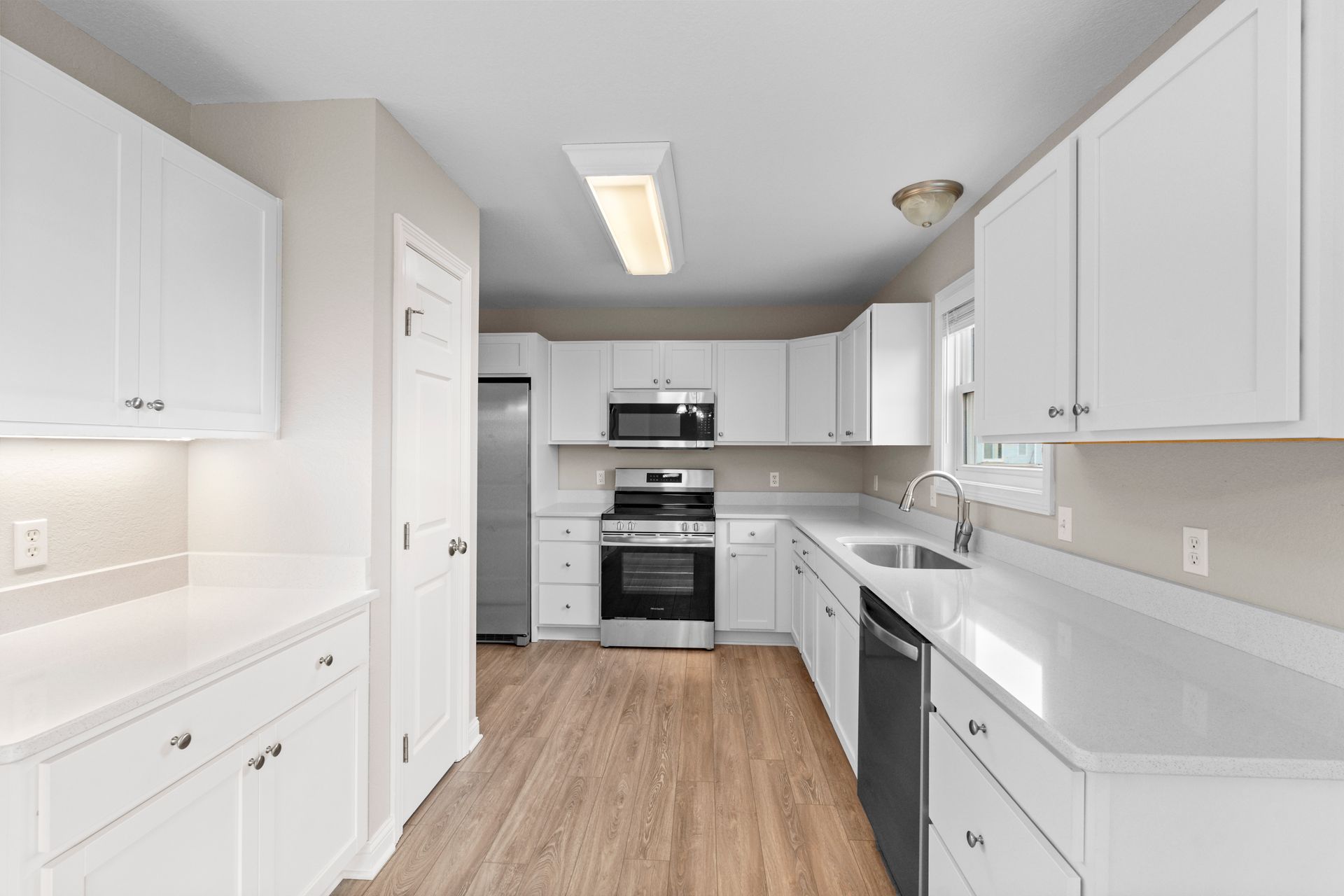 White kitchen with white cabinets, stainless steel appliances, and wood-look flooring.