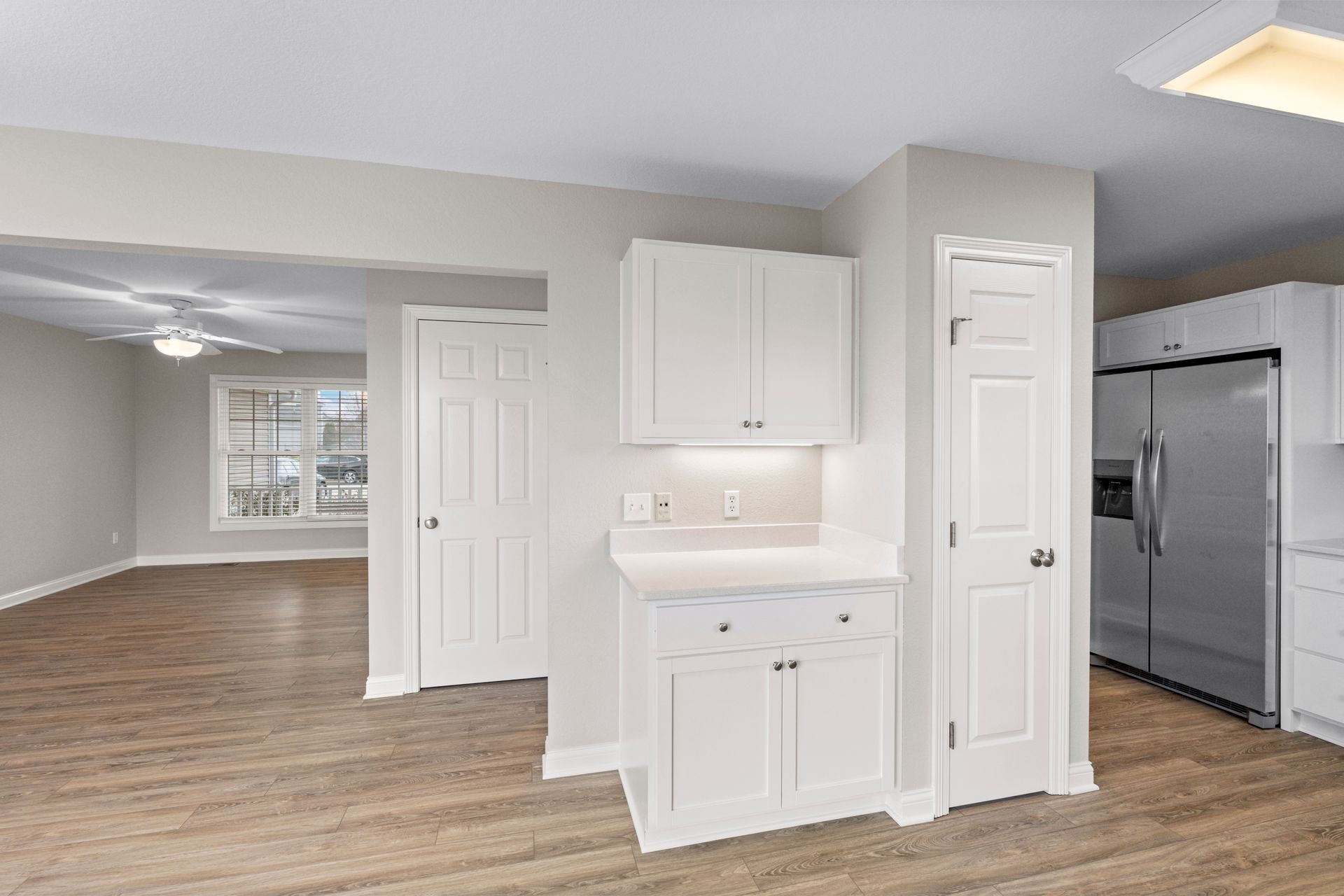 Kitchen and living area with white cabinets, stainless steel refrigerator, and wood-look flooring.