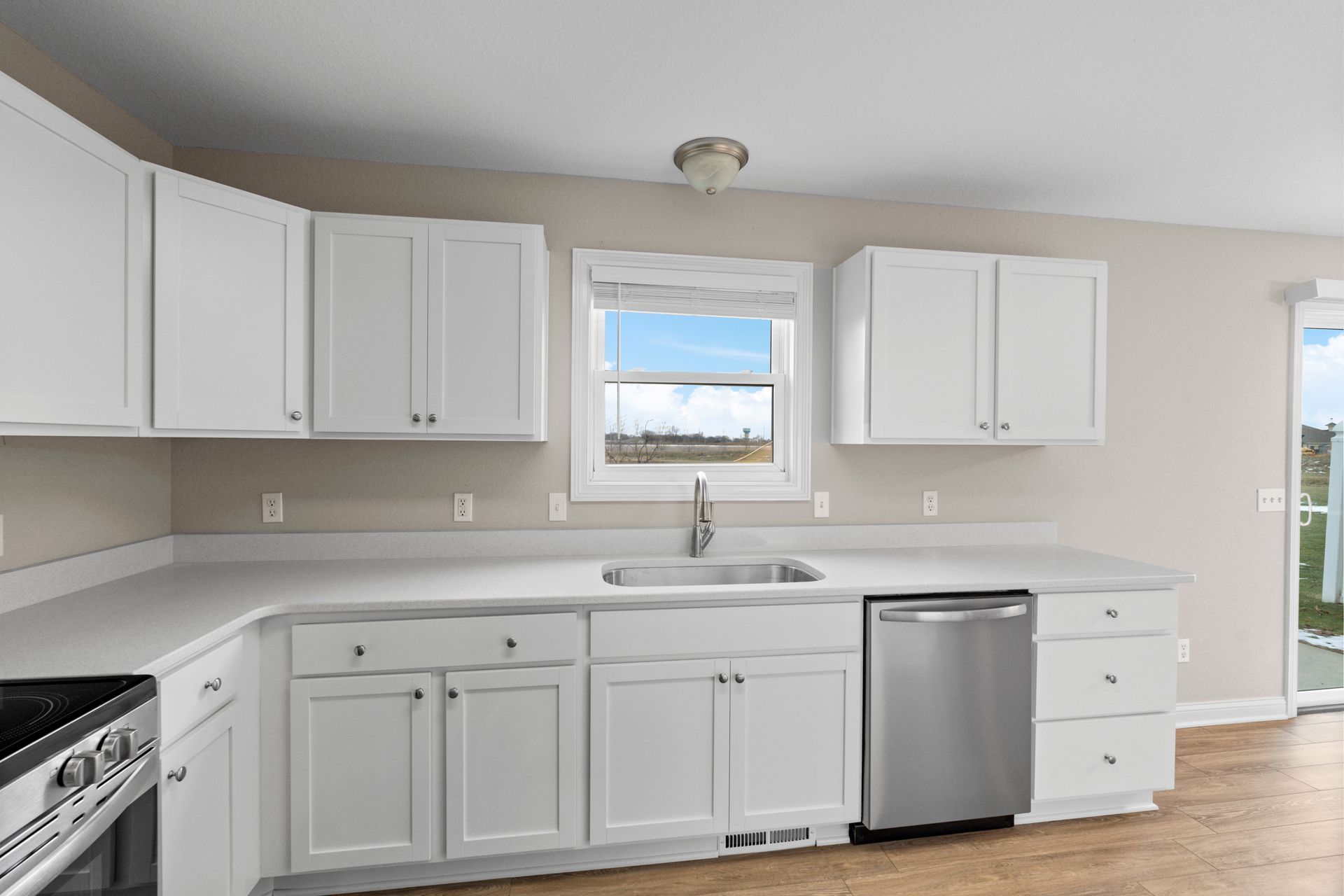 White kitchen cabinets with stainless steel appliances, sink in front of a window.