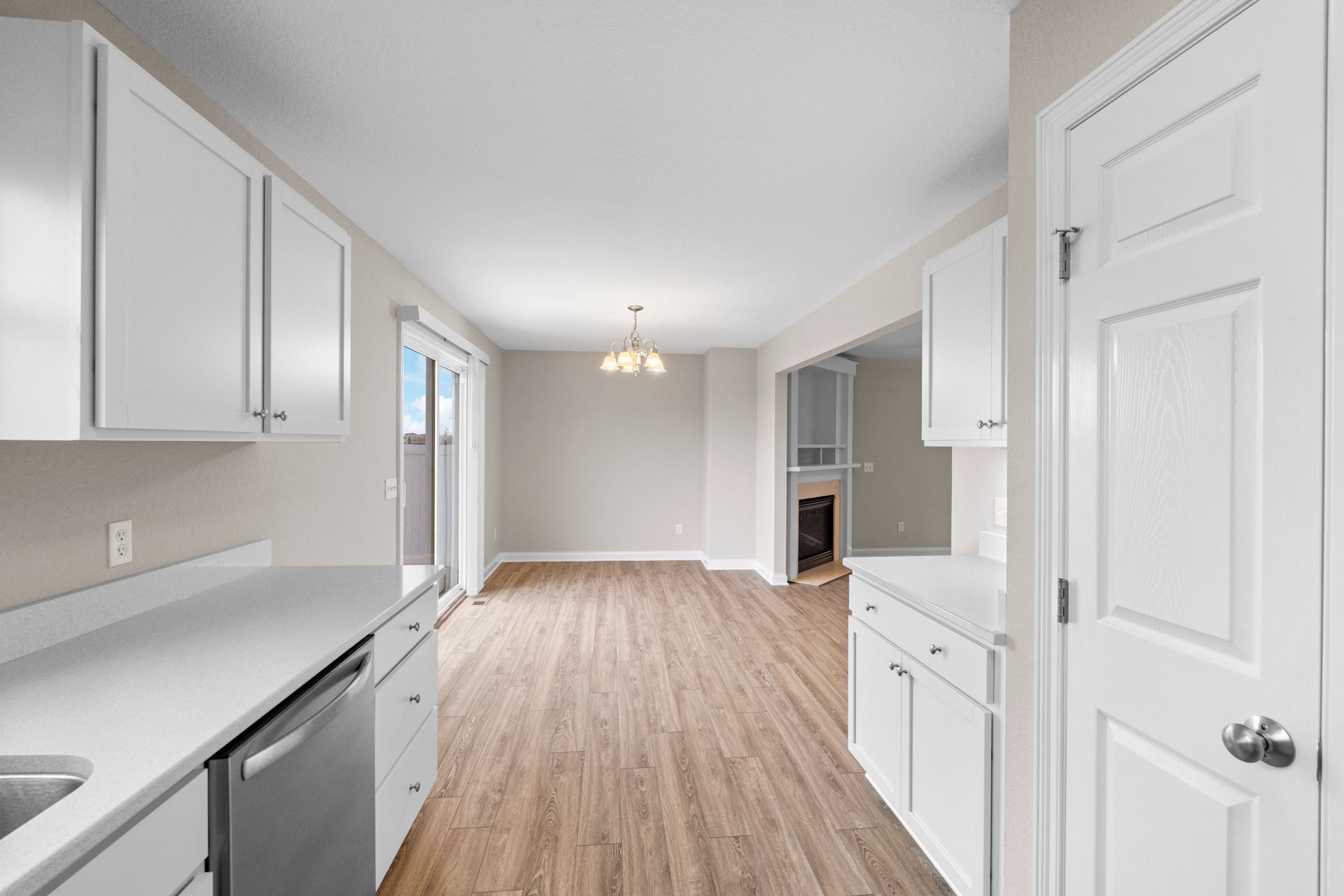 Kitchen with white cabinets and countertops, looking into dining area with hardwood floors.