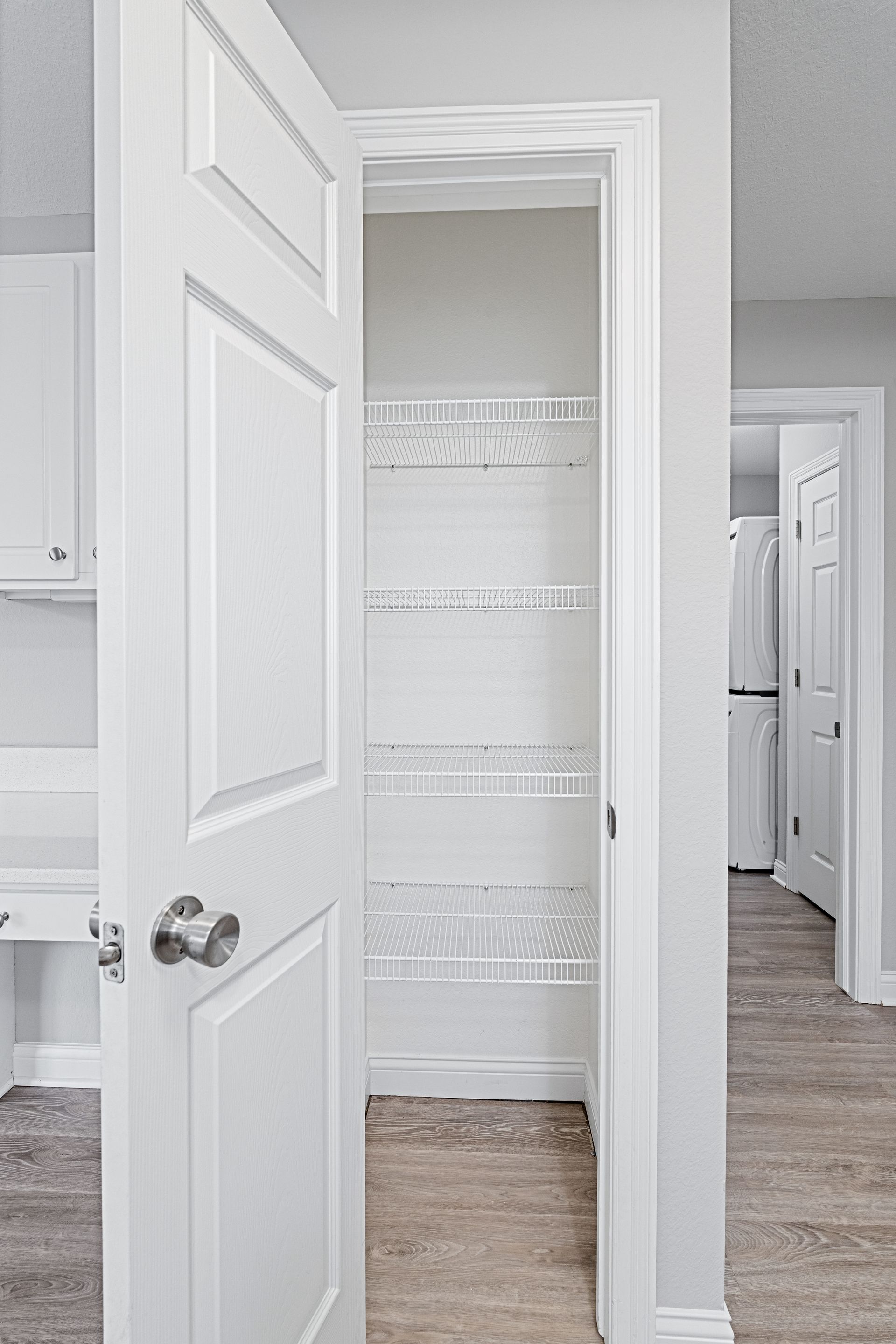 White pantry with wire shelves, door slightly ajar, visible in a neutral-colored hallway.