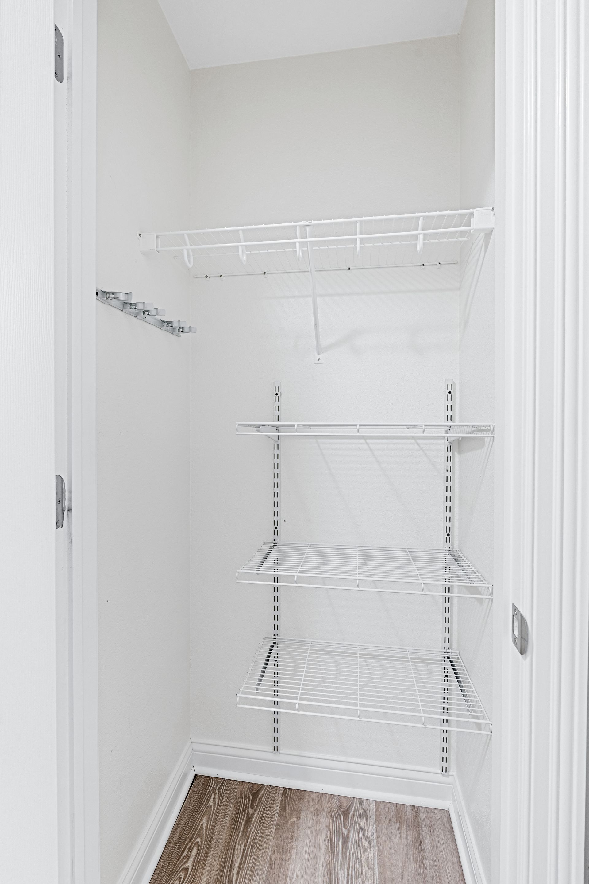Empty white pantry with wire shelves, dark wood-look flooring.