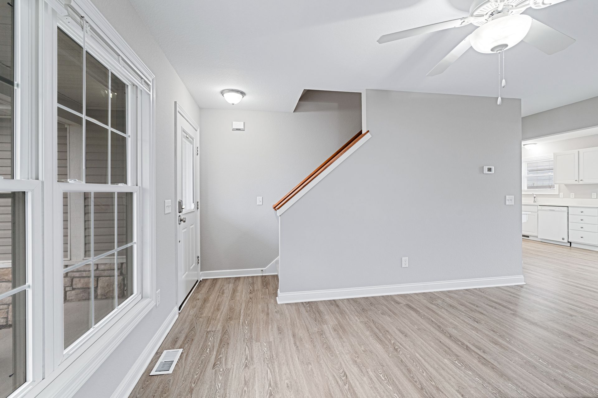 Living room with gray walls, wood-look flooring, stairs, and a window.