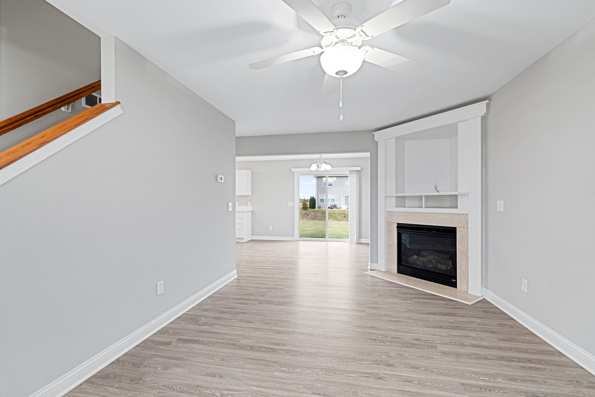 Living room with gray walls, wood-look flooring, fireplace, stairs, and sliding glass door to a yard.