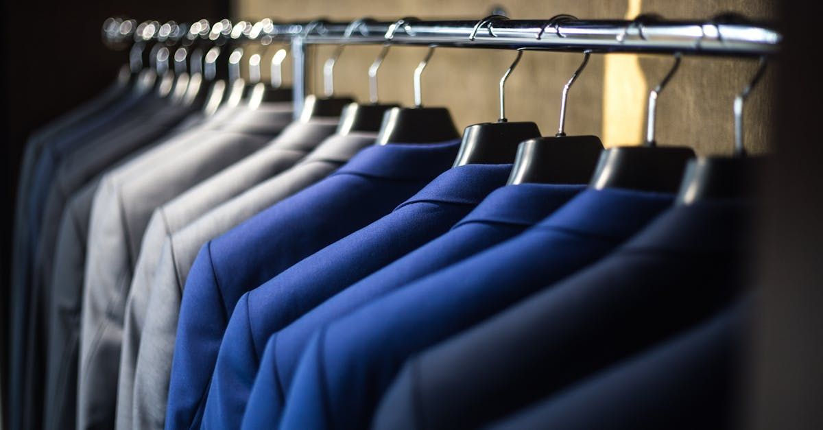 A row of suits hanging on a rack in a closet.