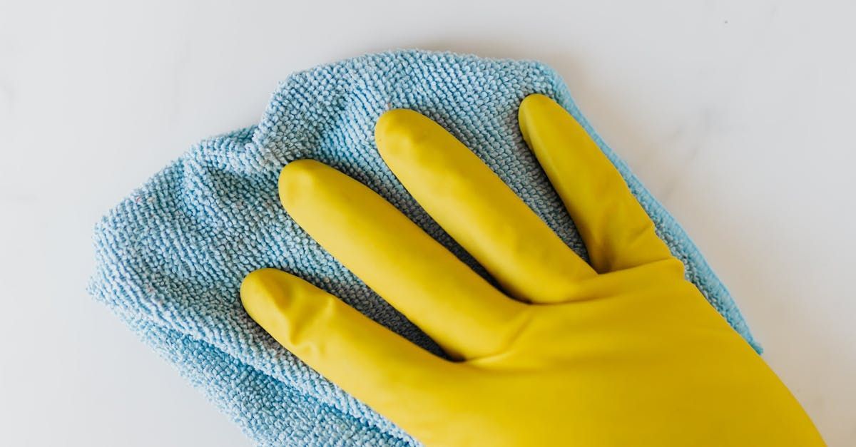 A person wearing a yellow rubber glove is cleaning a white surface with a blue cloth.