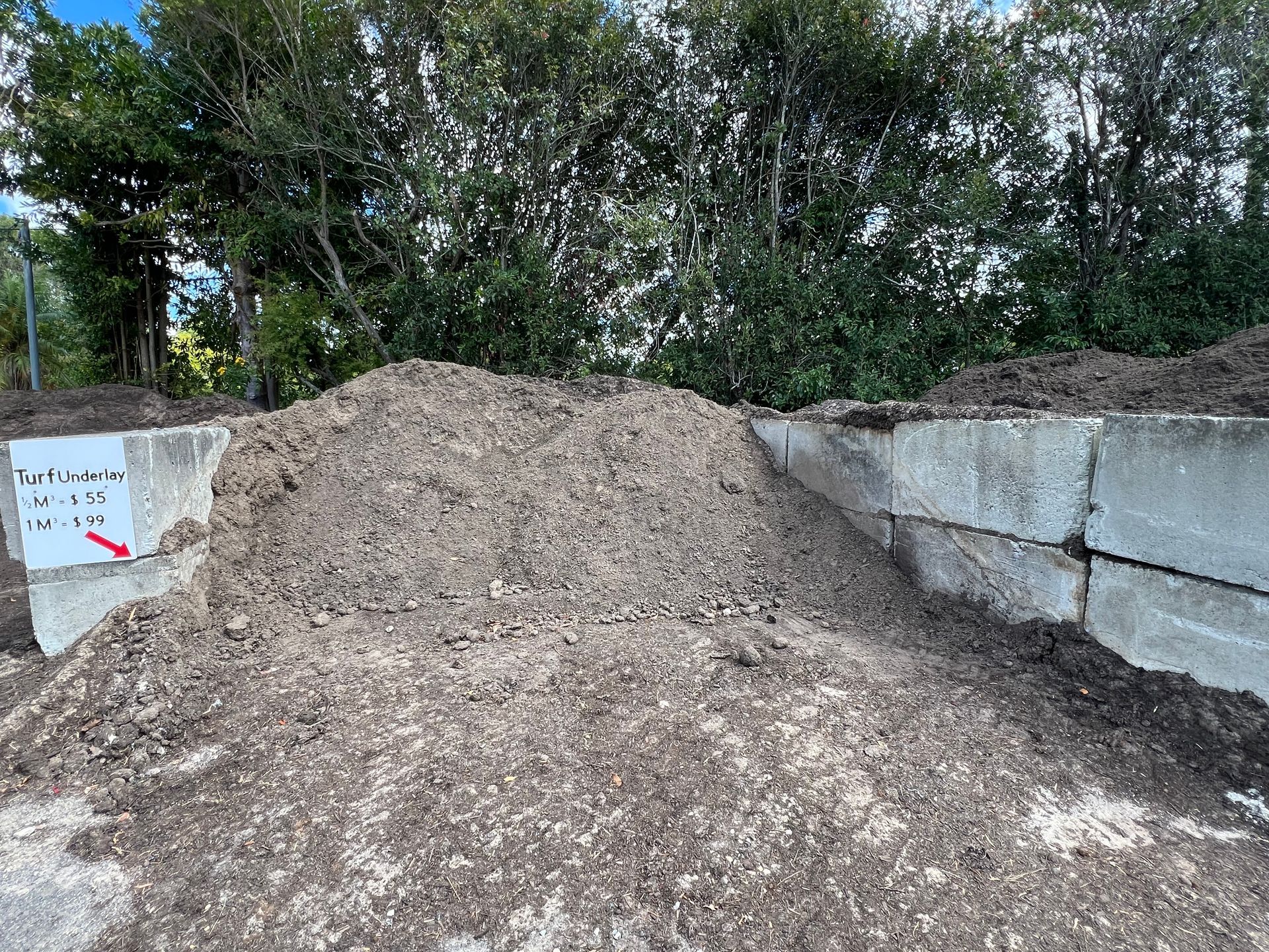 A large pile of mulch sits in a concrete bin outdoors, with a small sign on the left indicating price and type — Laurieton Landscape Supplies In Kew, NSW