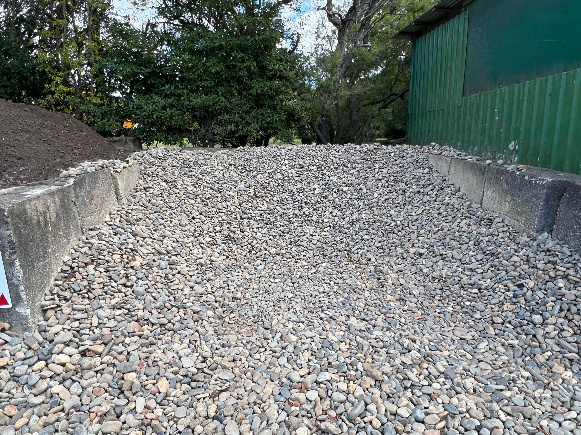 A pile of grey gravel stones contained within a concrete enclosure — Laurieton Landscape Supplies In Kew, NSW