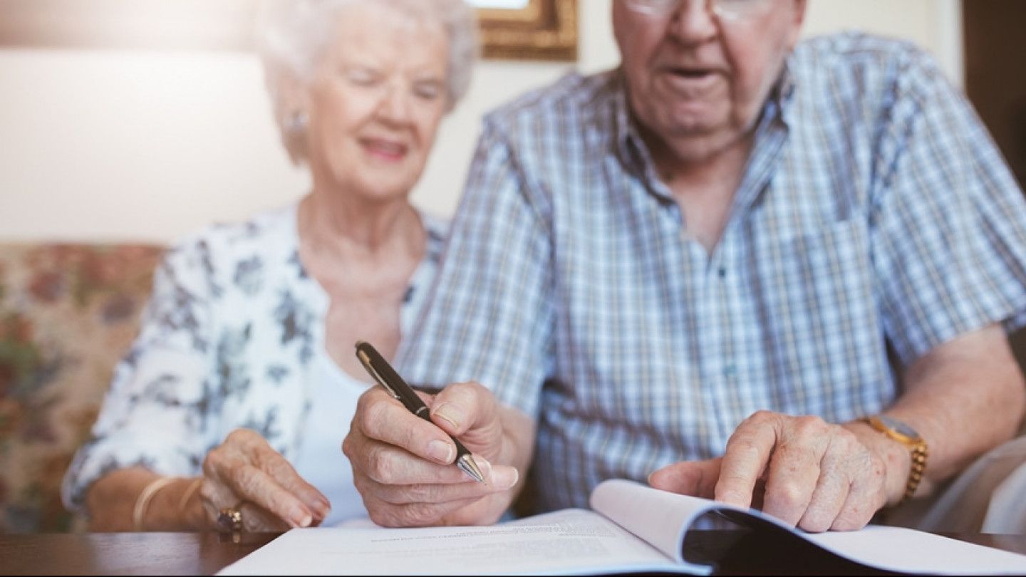 An elderly couple is sitting at a table signing a document