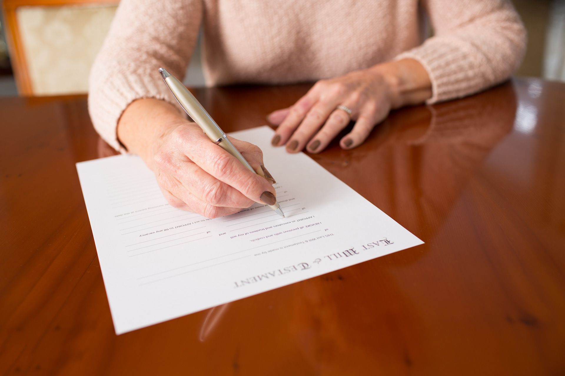 A woman is sitting at a table writing on a piece of paper with a pen