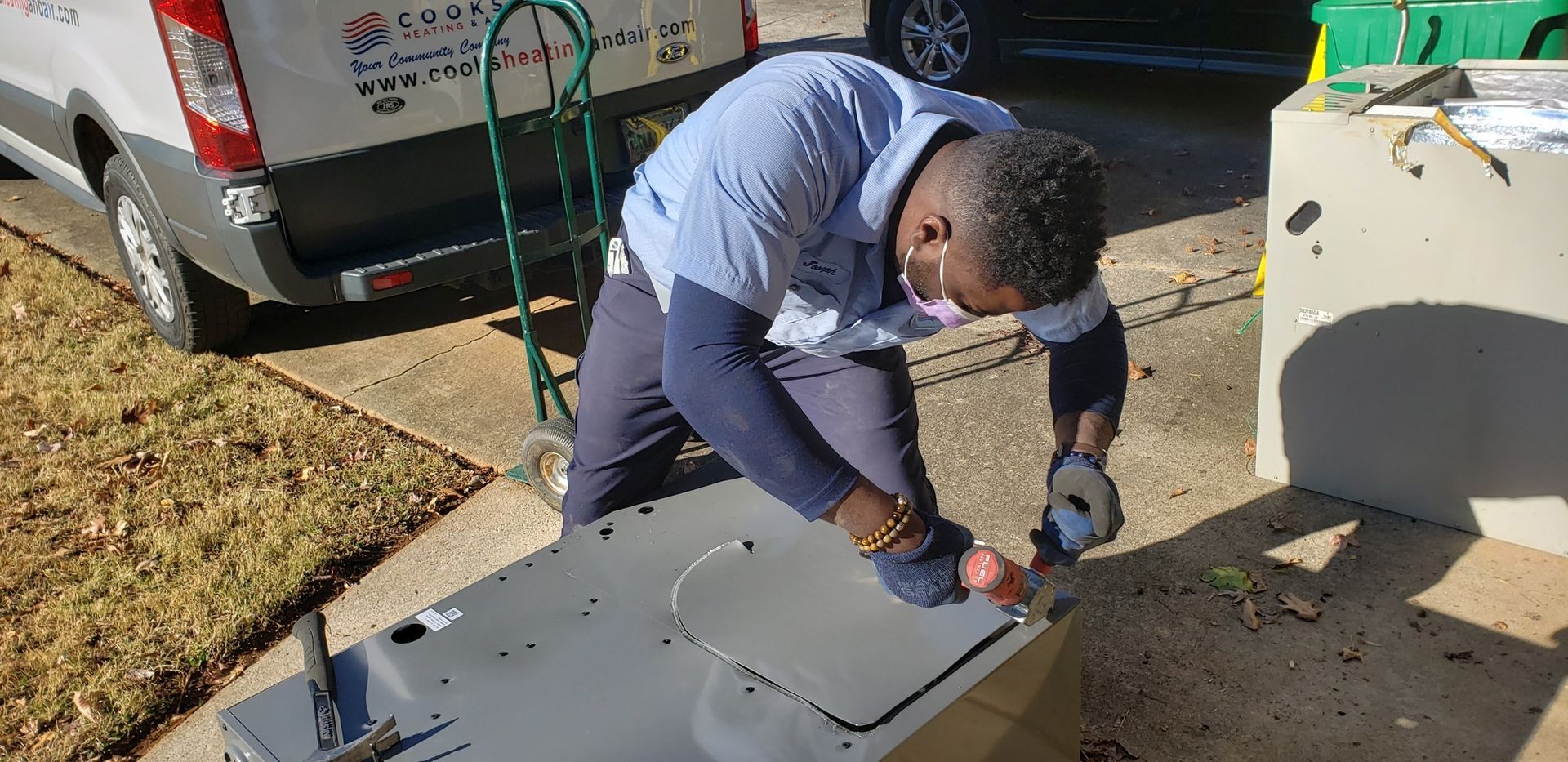 A man is kneeling on the ground working on a piece of metal.