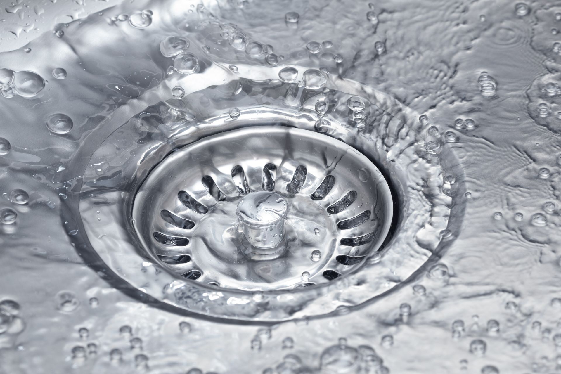 Water flowing into a stainless steel kitchen sink drain.