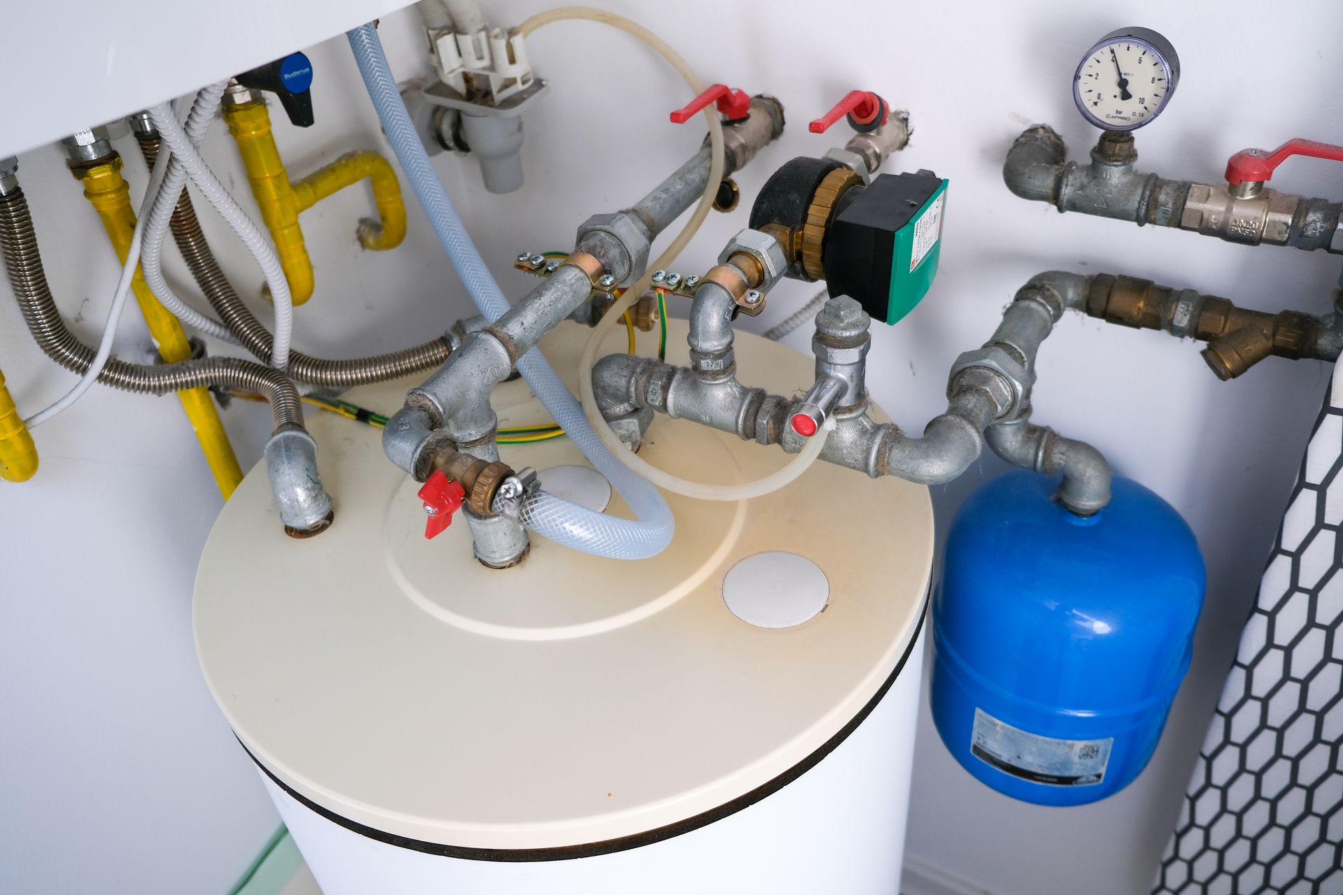 White water heater with connected pipes, valves, and a blue expansion tank against a white wall.