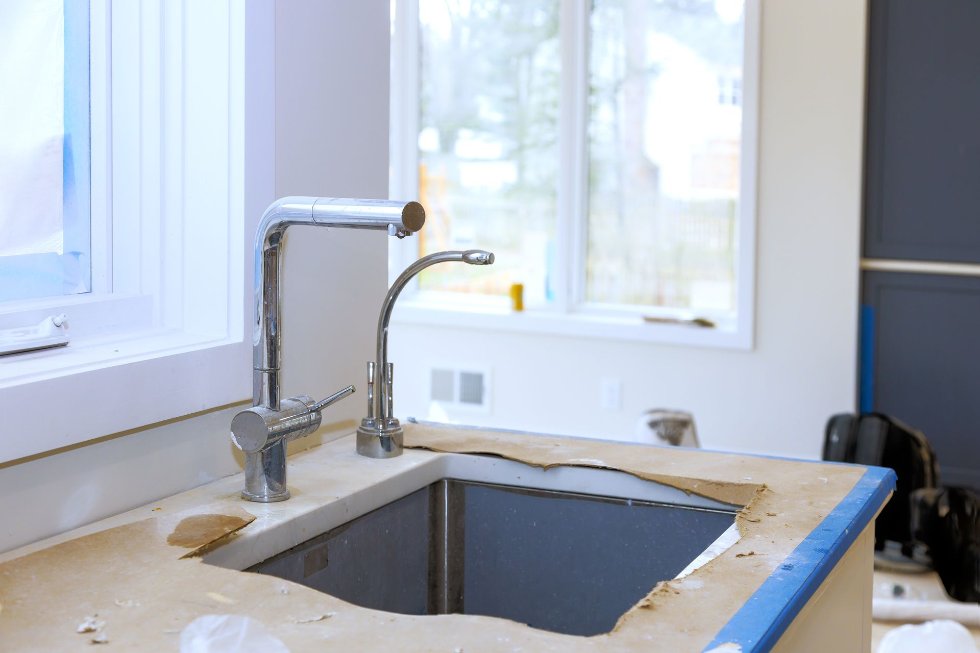 New kitchen sink with chrome faucet. Countertop under construction with window in background.