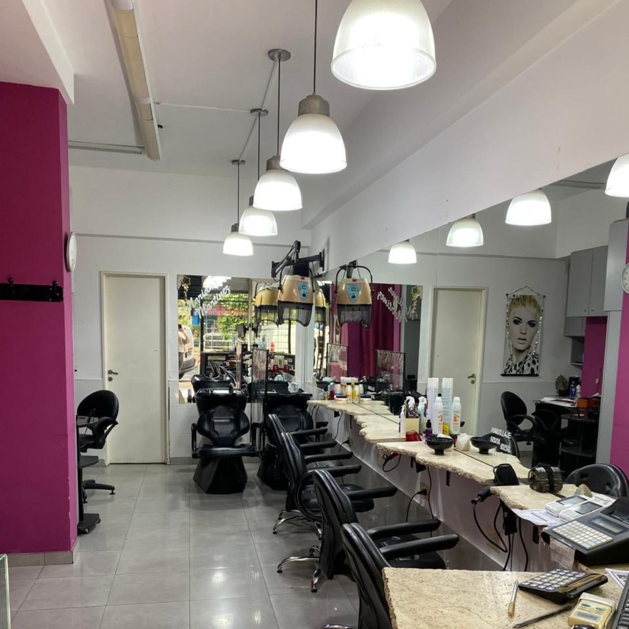 Interior de peluquería: sillas, espejos y detalles en rosa. Luces cenitales iluminan el espacio.